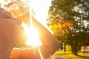 A person outdoors holding a water bottle to their head during a sunny day